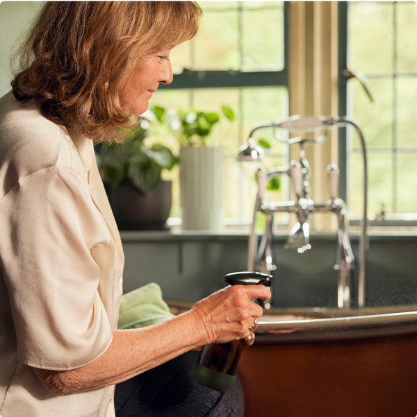 Co-founder Purdy holds a bottle of Purdy & Figg and a cloth against the backdrop of a beautiful bathroom.