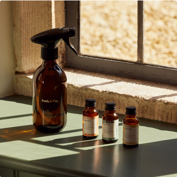 A Purdy & Figg glass spray bottle and three small refill bottles in a row, lit by warm sunlight on a sea green window ledge. 