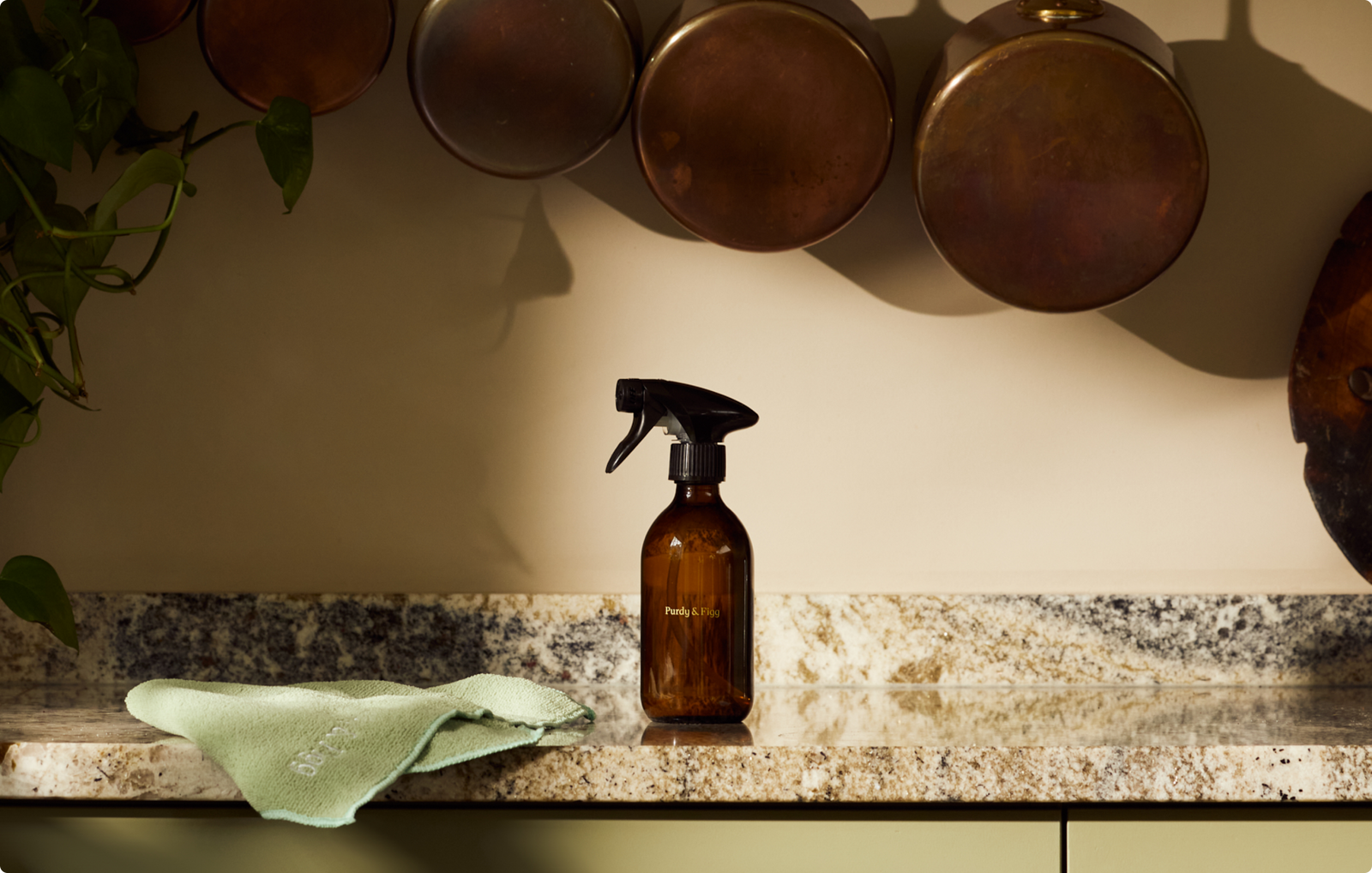 Bottle for Life and Cloth on a marble work top, with metal saucepans hanging up behind