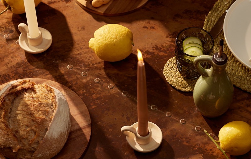 Lighted candle on table, surrounded by freshly baked bread and fruits