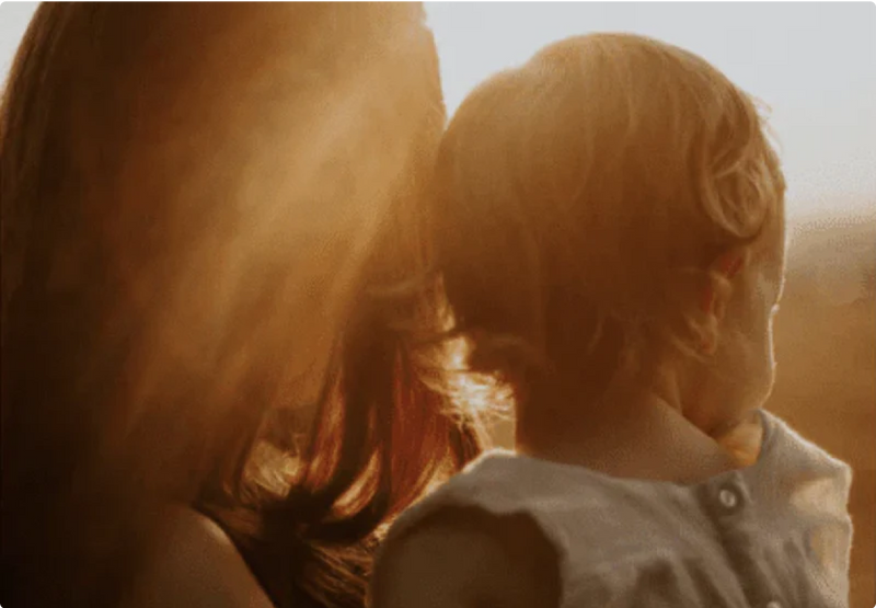 A woman holding a child, looking into a beautiful late afternoon sun