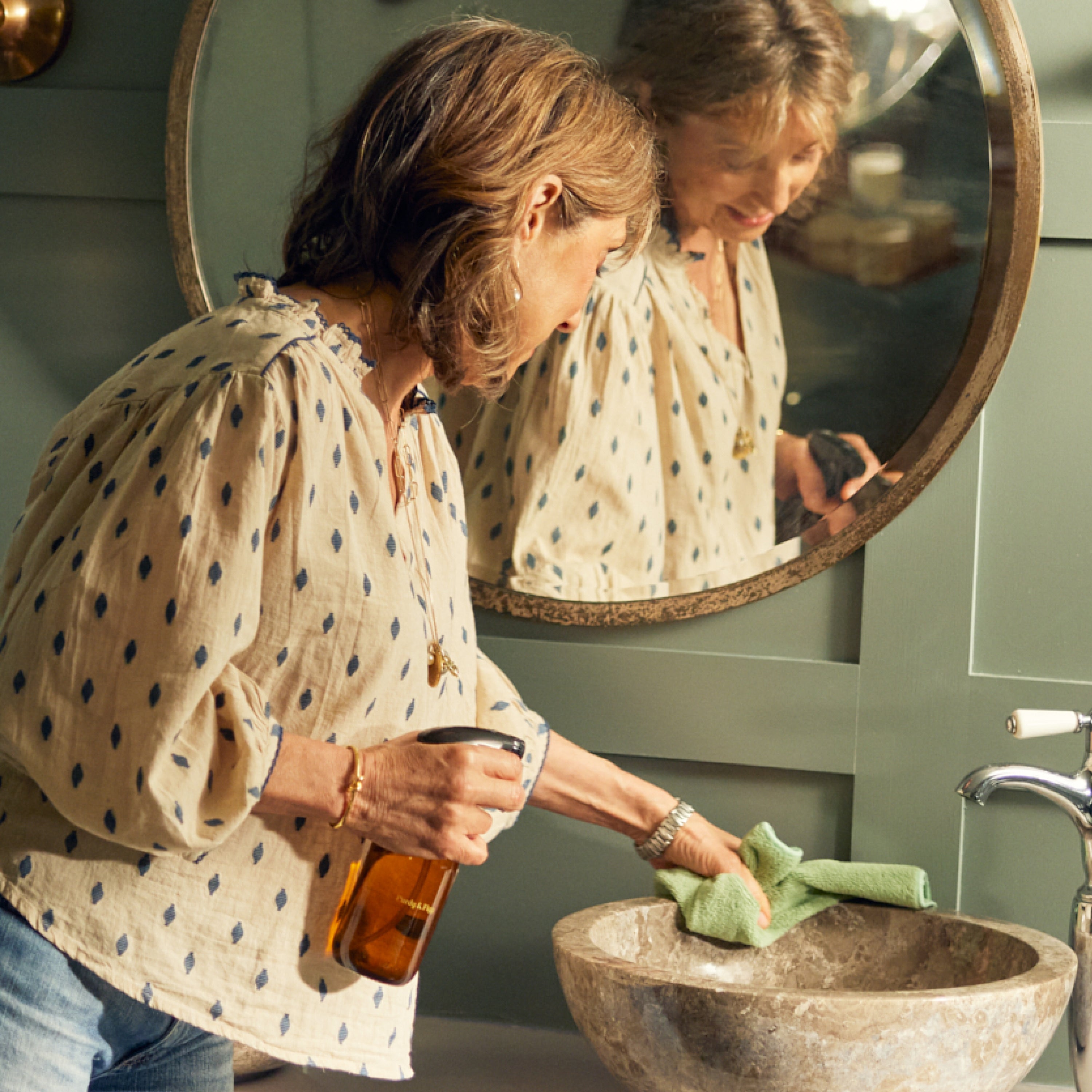 Charlotte cleans a beautiful marble sink, in front of a circular mirror