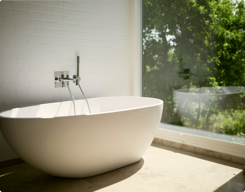 A free standing bath tub next to a window looking out on leafy trees