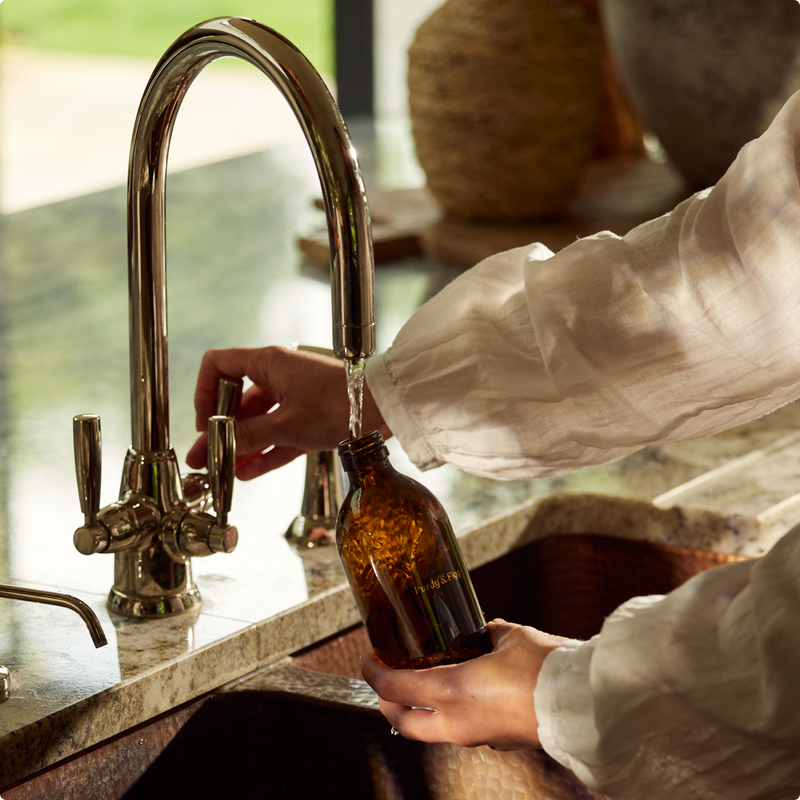 A woman fills a bottle from a tap over a beautiful sink