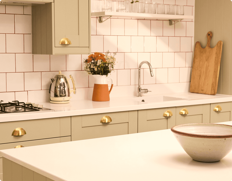 Bright and airy kitchen, with flowers on a white table-top in front of white tiles.